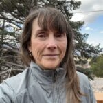 Woman in gray jacket outdoors by tree