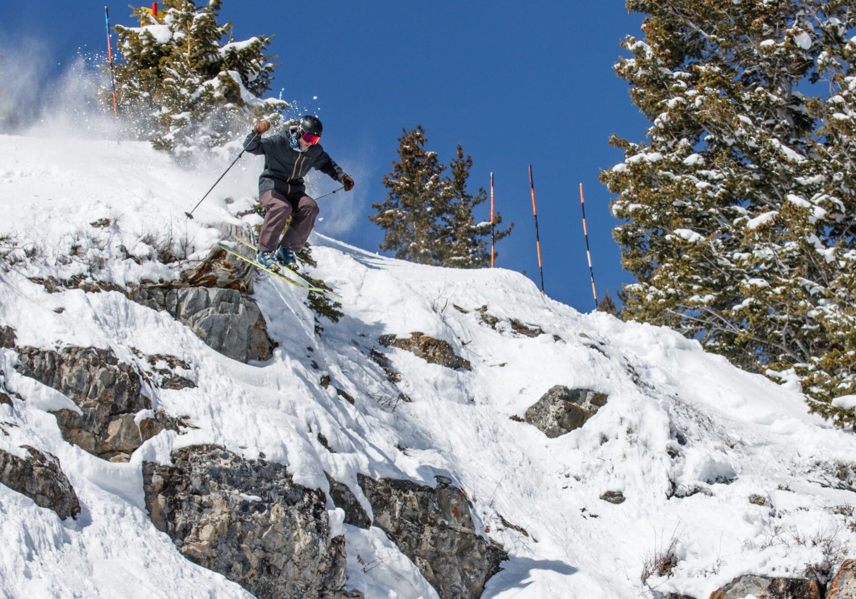 Skier launching off snowy cliff under blue sky